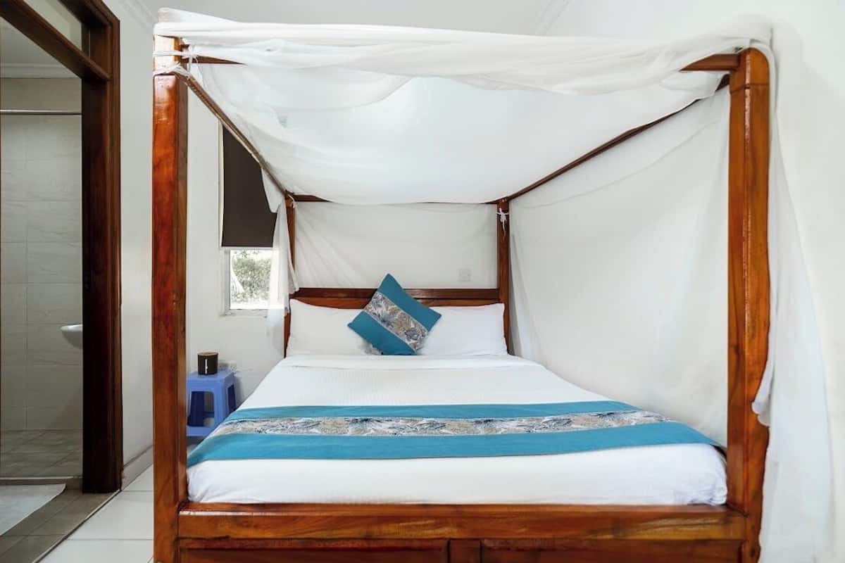 A four-poster bed with a canopy, white linens, a blue and white throw, and a blue stool beside the bed.