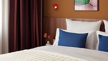 Una cama bien tendida con un juego de almohadas blanco y azul, un cabecero de madera y una lámpara fijada a la pared.