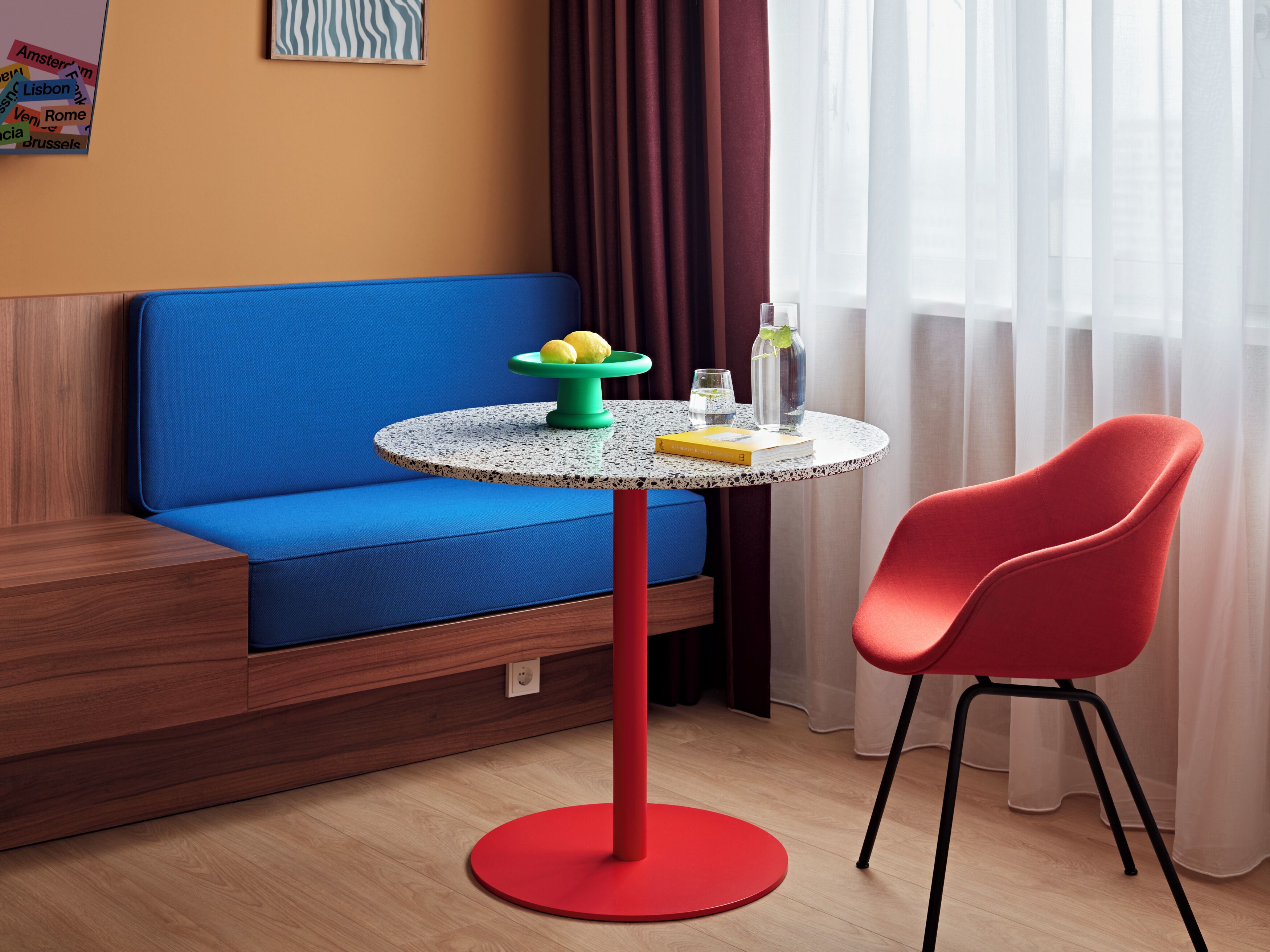A modern room with a blue sofa, a red chair, a round table with a green base, and a small green table with lemons and a book.