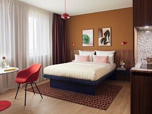 A hotel room with a bed, a red chair, a small table with a glass and a book, and a nightstand with a lamp. - Numa Hamburg St Georg (Hamburg)