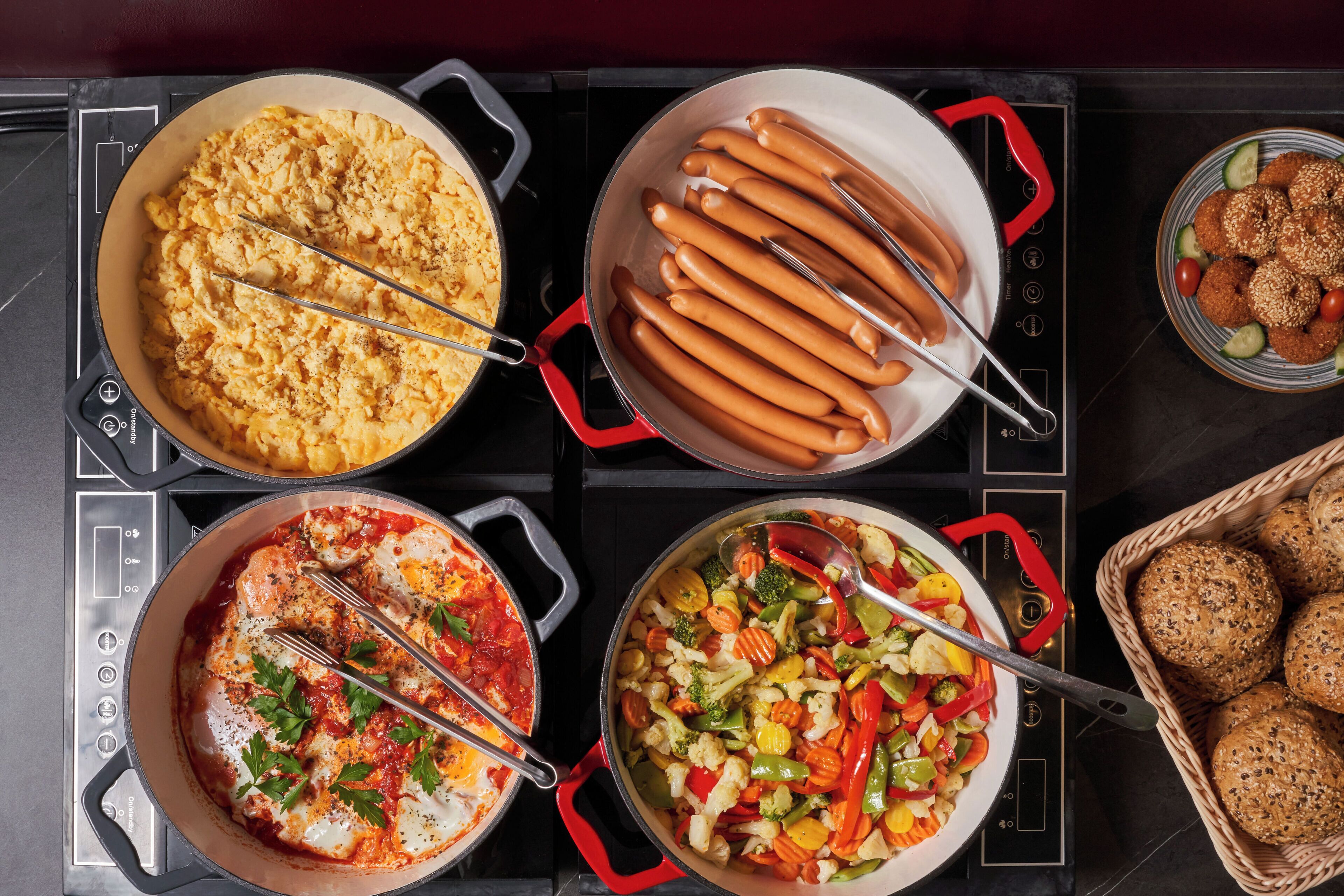 A kitchen with four pots on an induction cooktop, each containing different dishes.