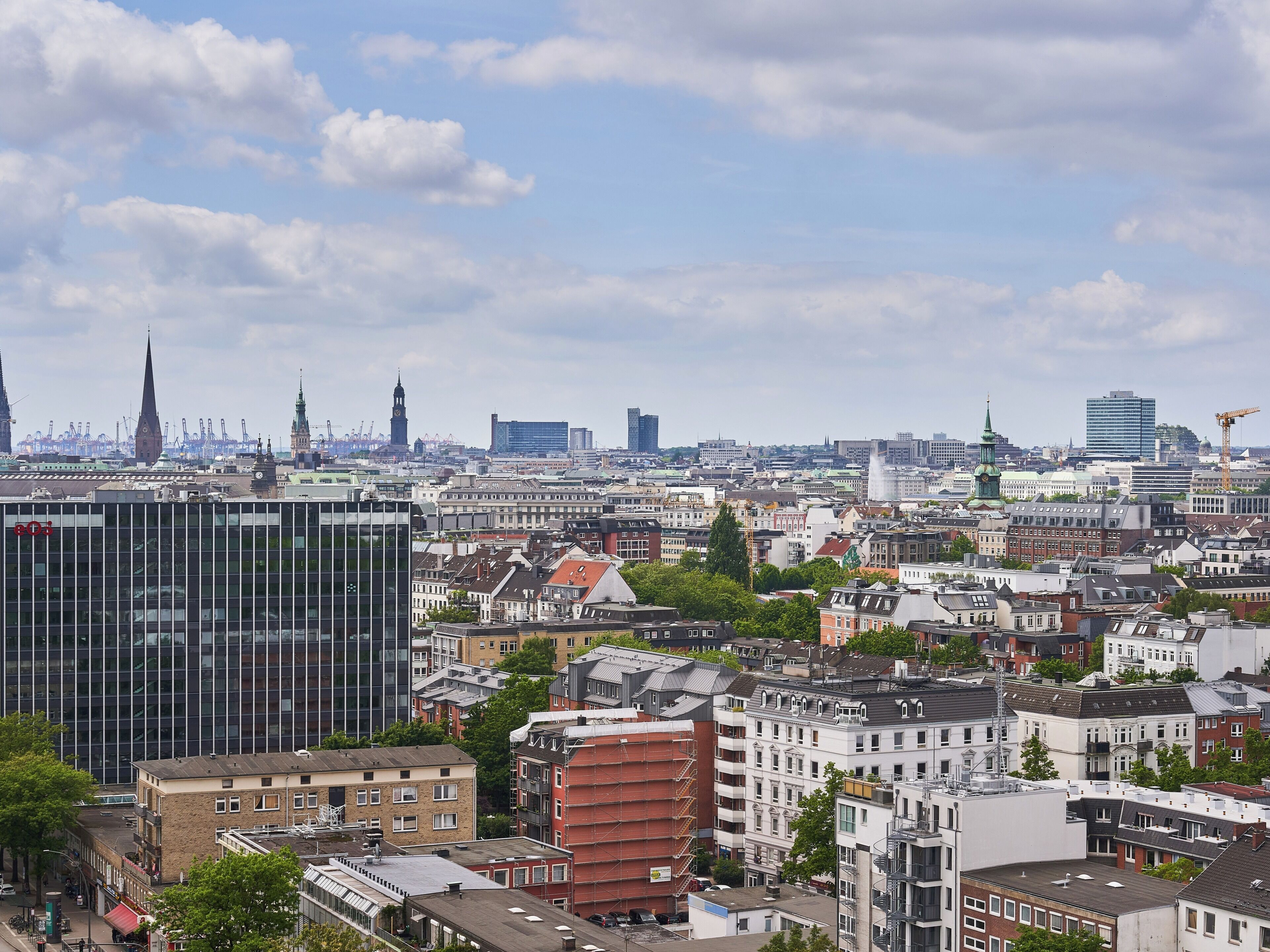 Un paisaje urbano con una mezcla de arquitectura moderna y tradicional, incluyendo una torre de reloj destacada y diversos estilos de construcción.