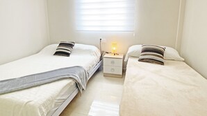 A twin room with two single beds, a bedside table with a lamp, and a window with blinds. - Beautiful apartment fully refurbished with lovely sea views. (La Manga del Mar Menor)