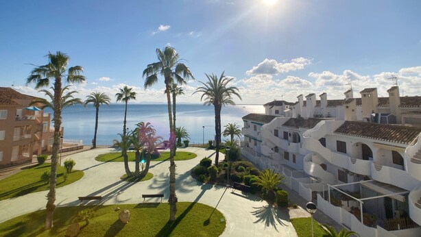 A resort with a pool, palm trees, and a view of the sea. - Beautiful apartment fully refurbished with lovely sea views. (La Manga del Mar Menor)