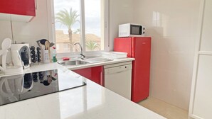 A kitchen with a white countertop, a red refrigerator, a microwave, and a window with a view of palm trees. - Beautiful apartment fully refurbished with lovely sea views. (La Manga del Mar Menor)