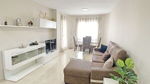 A modern living room with a sofa, TV, and a dining area with a table and chairs. - Beautiful apartment fully refurbished with lovely sea views. (La Manga del Mar Menor)