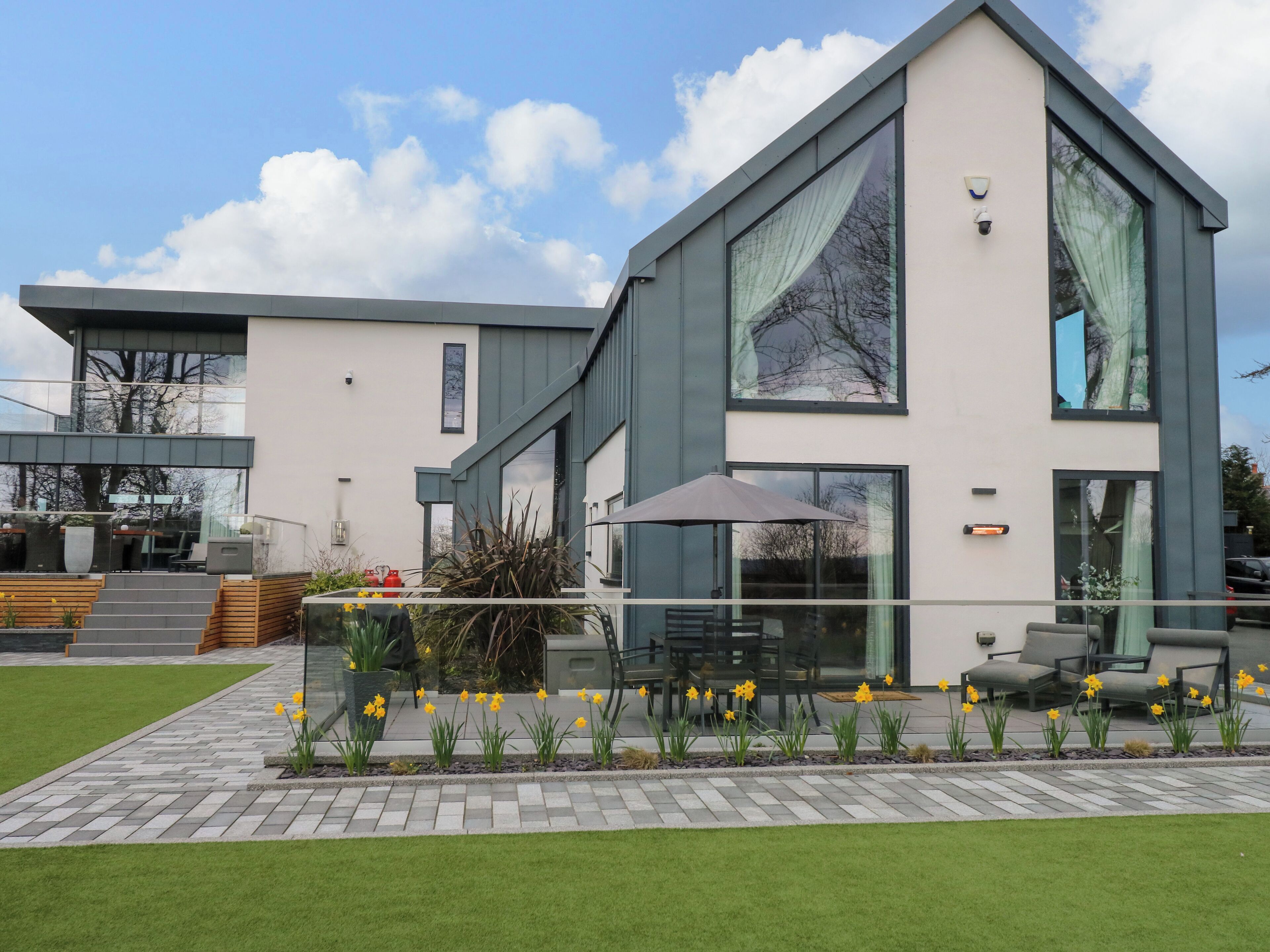 A modern two-story house with a patio area featuring outdoor seating and daffodils.