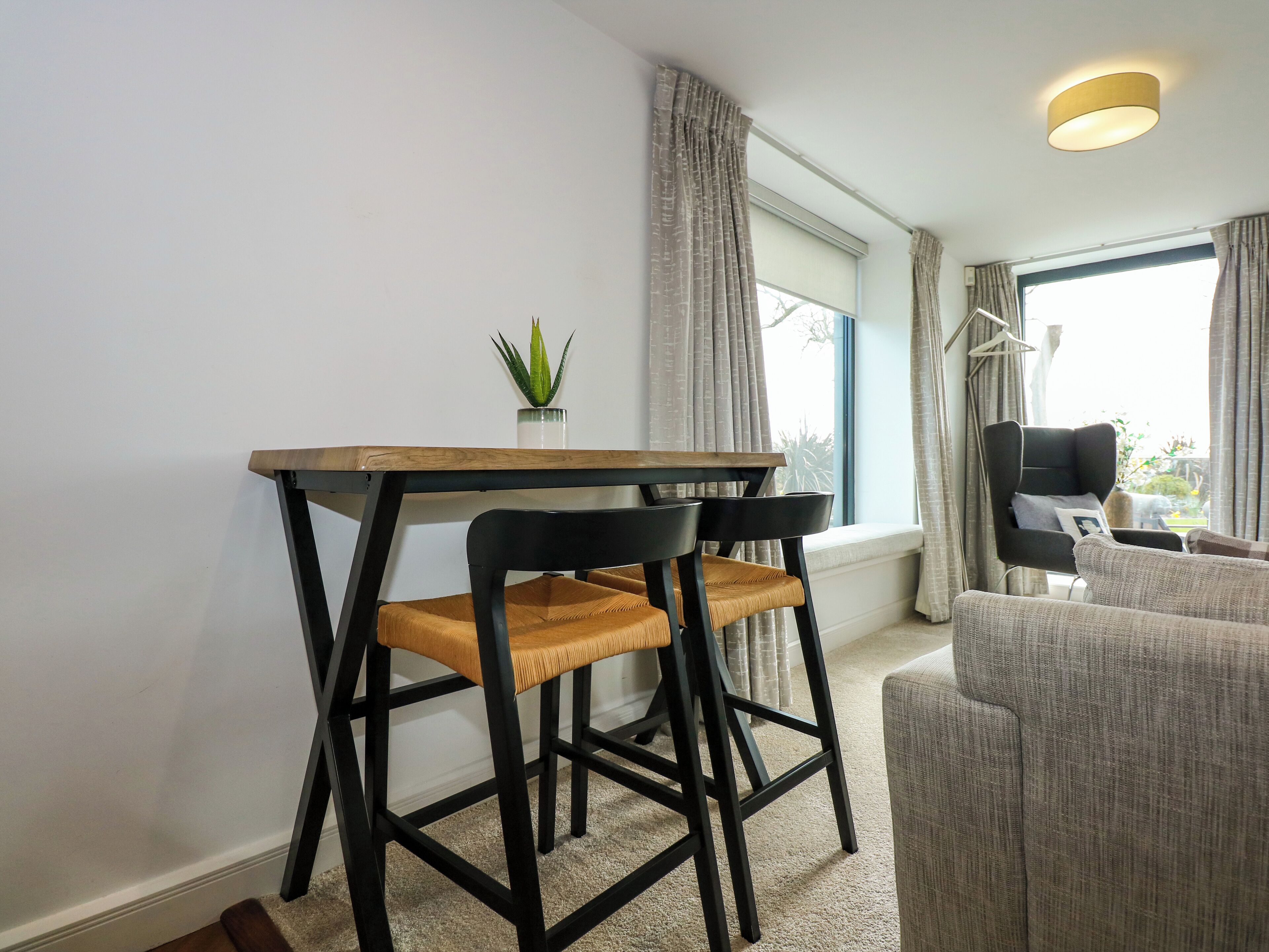 Un salon moderne avec une table à manger en bois, deux chaises noires, un canapé gris et une plante en pot.