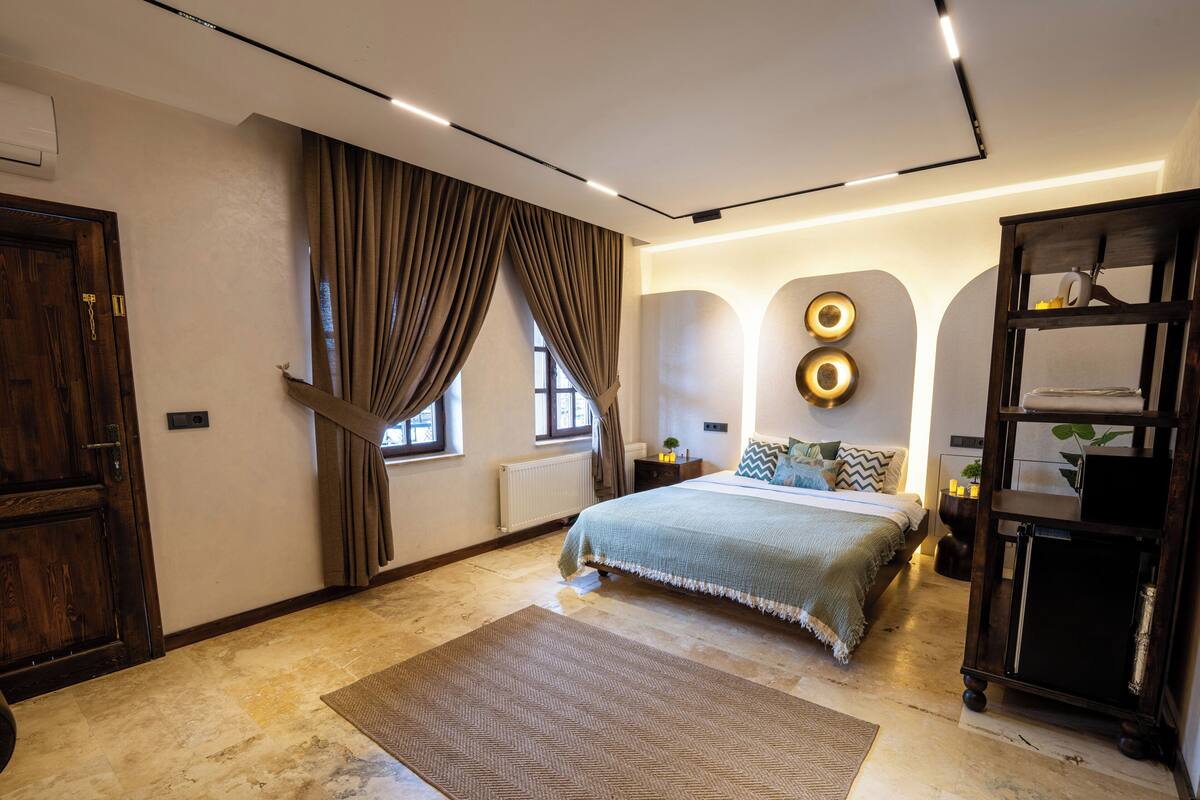 Un dormitorio con cama, un armario de madera, un radiador y un amplio ventanal con cortinas.