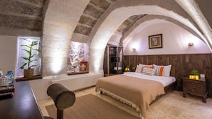 Quarto com teto abobadado, cama, mesas de cabeceira, radiador e janela com planta.