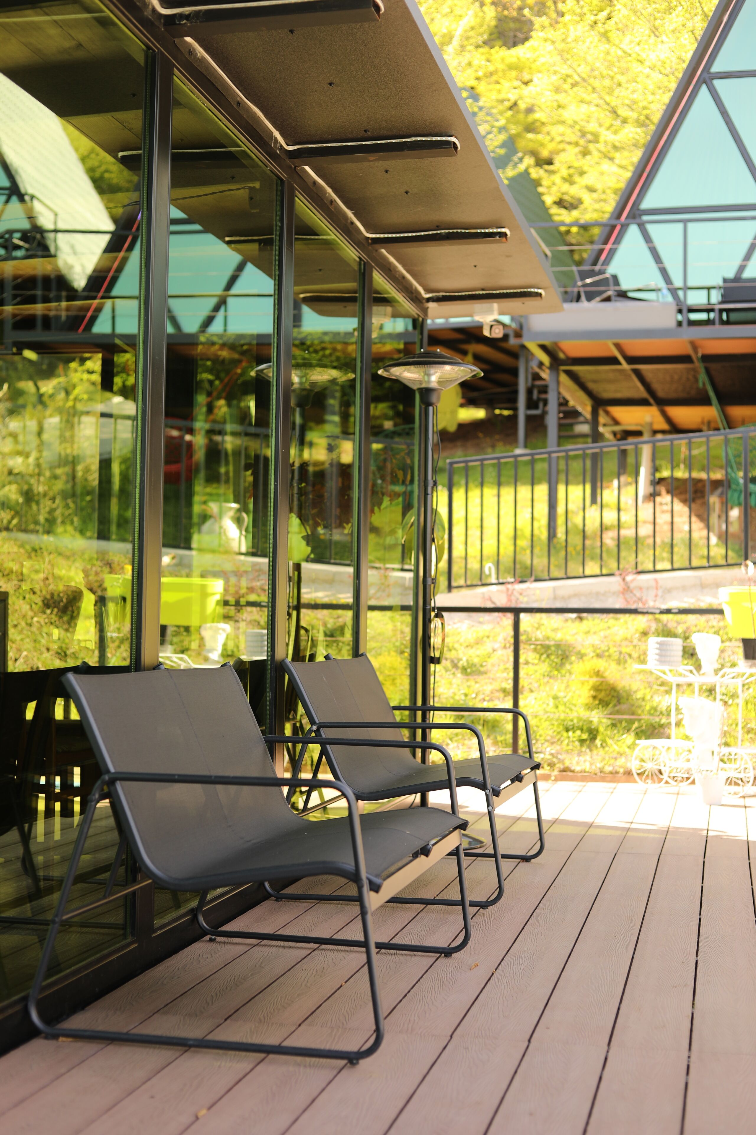 Terraza con dos sillones de descanso y una mesa, con vista a un jardín y un edificio con amplios ventanales.