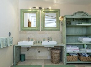 Une salle de bain avec deux lavabos, un grand miroir et une étagère où sont rangées les serviettes et les articles de toilette.