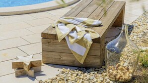 Un banc en bois avec des serviettes, une bouteille de vin et une décoration en forme d’étoile près d’une piscine.