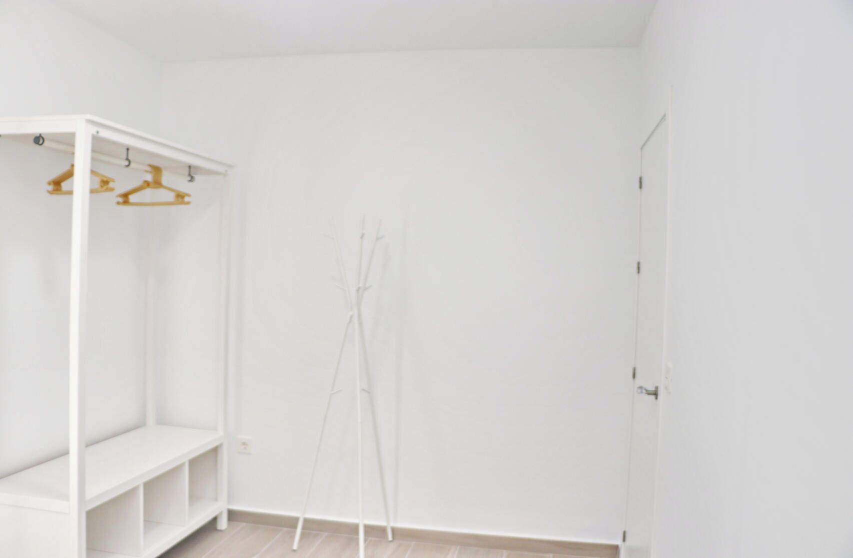 Ein weißes Zimmer mit einem Schrank, der Regale und Holzaufhänger enthält.