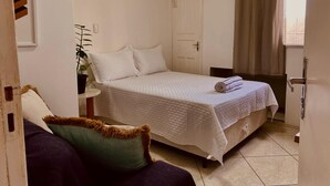A small, neatly arranged bedroom with a bed, a chair, a potted plant, and a window with curtains. - Loft CeoPremium 2 | near beaches and shopping malls (Salgado Filho Aracaju)
