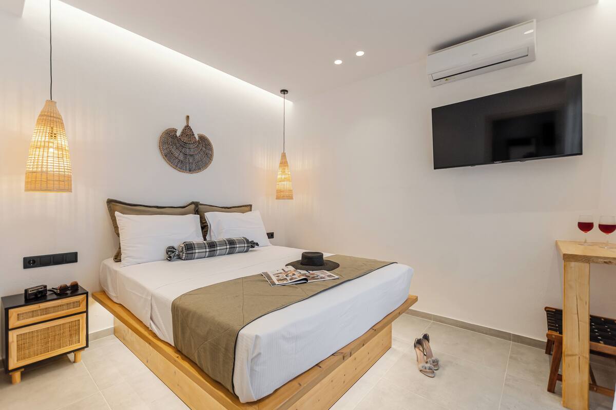 A modern bedroom with a bed, bedside tables, a TV, and a small wooden table with glasses.