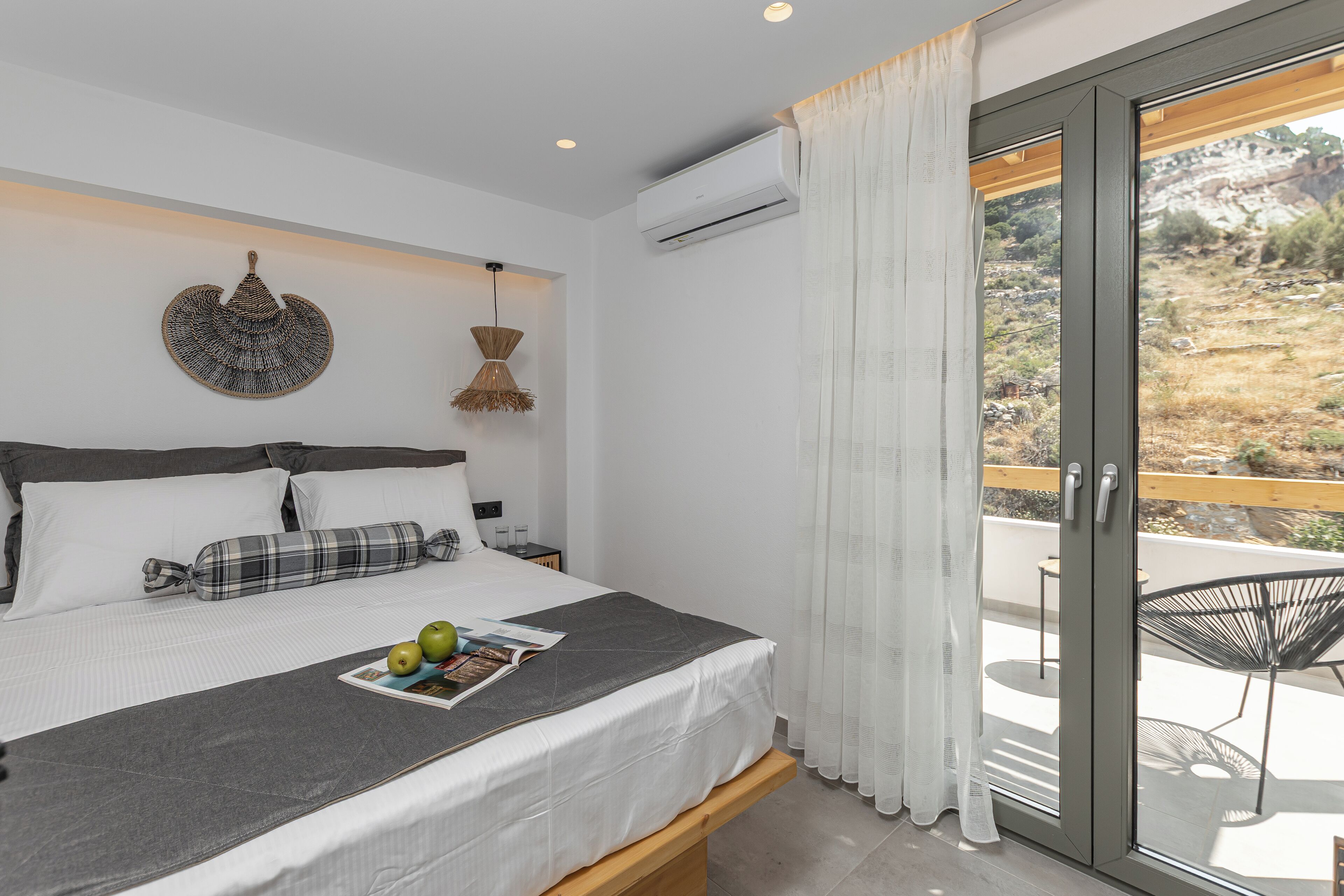 Camera da letto con un letto, un comodino, una lampada a sospensione e vista sull'esterno attraverso una porta scorrevole in vetro.