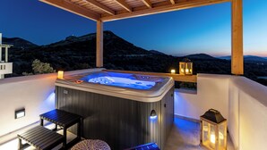 Ein Whirlpool mit einer Holzpergola, einem kleinen Tisch und einer Laterne auf einem Balkon mit Blick auf eine gebirgige Landschaft.