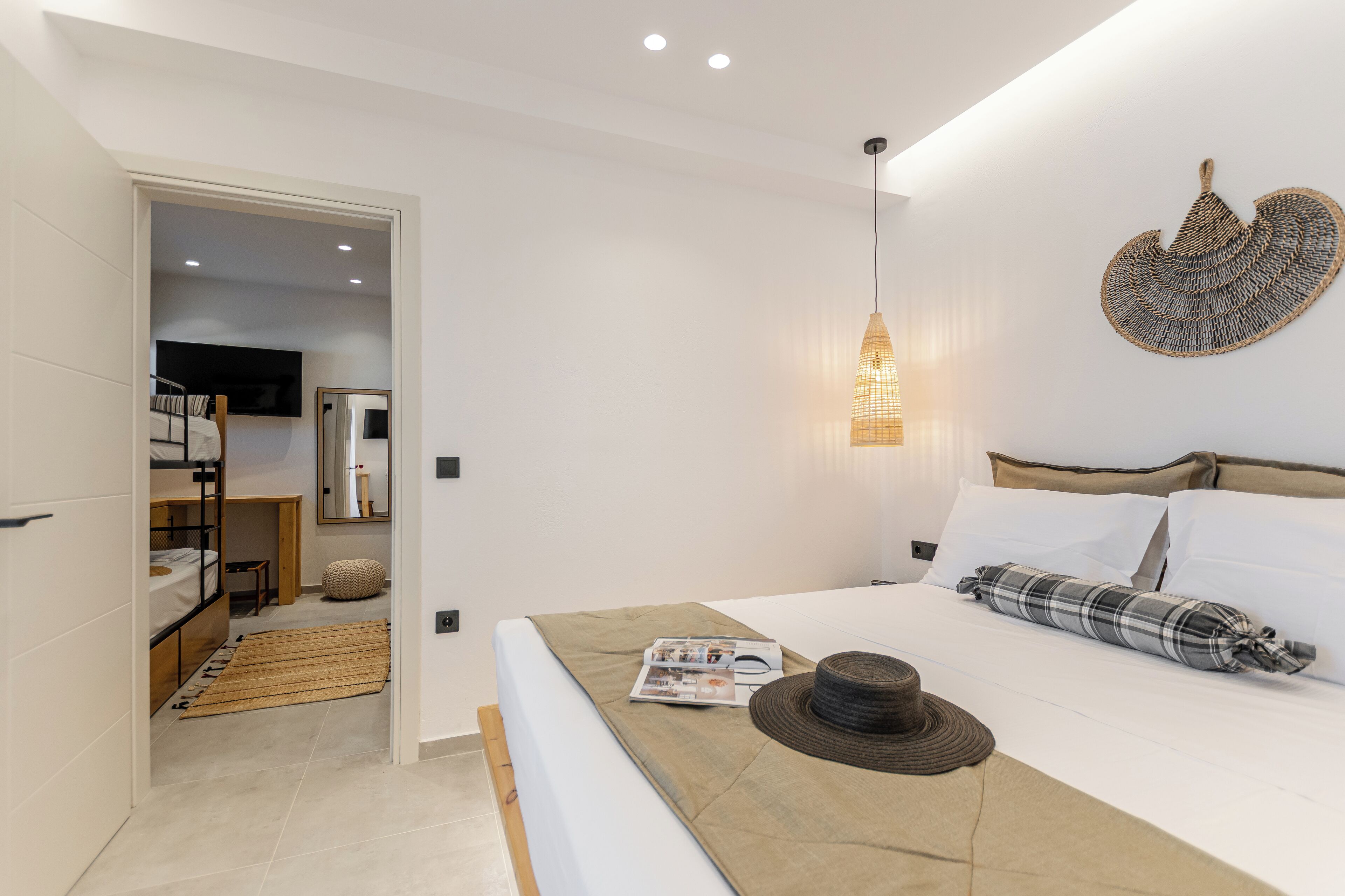 A modern bedroom with a bunk bed, a bedside table with a magazine, a hat, and a wall-mounted light fixture.