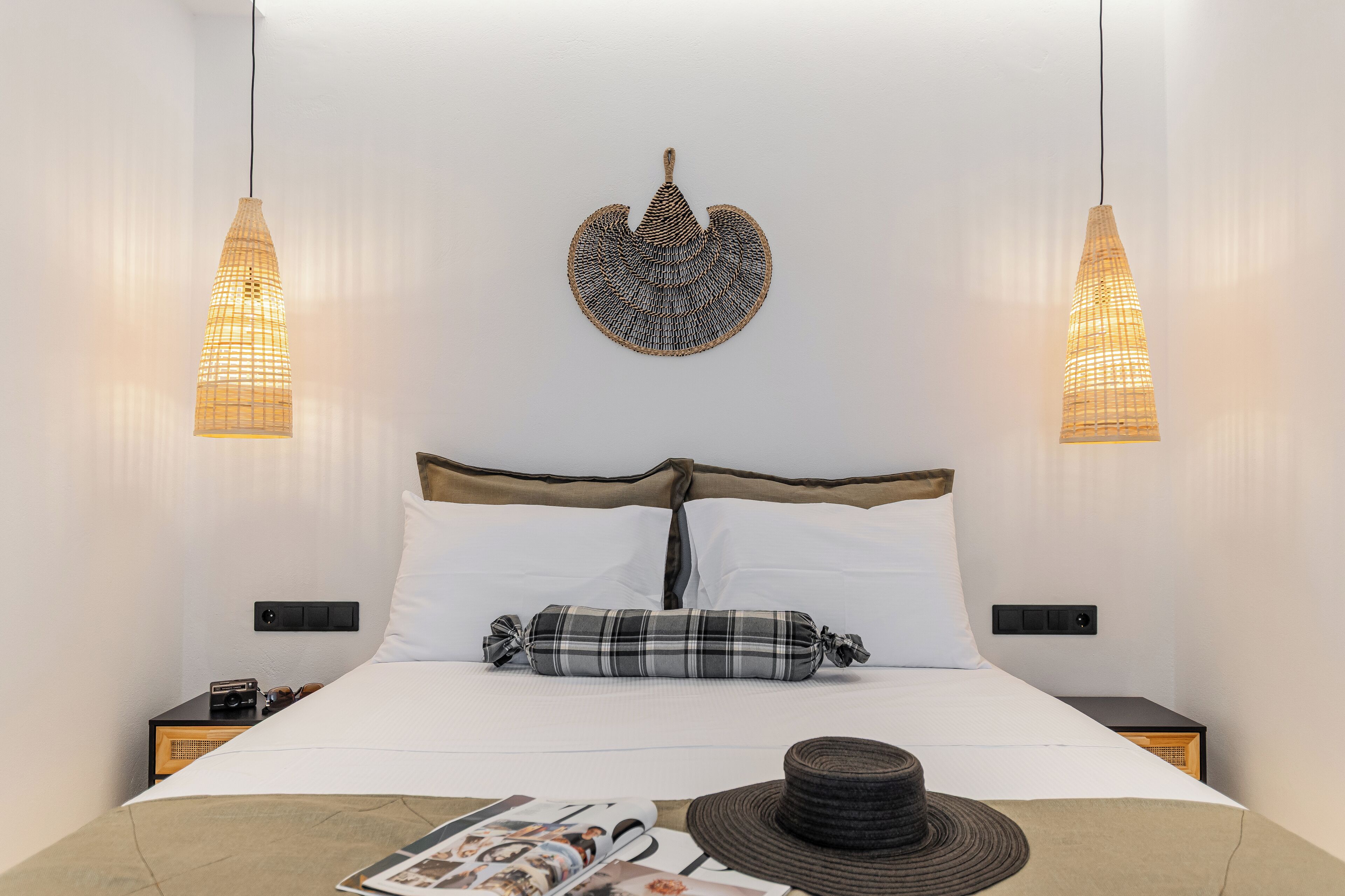 A neatly made bed with a headboard, two bedside tables, a magazine, and a hat on the bed.