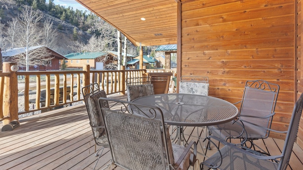 Una terraza de madera con sillas y una mesa de metal, con vistas a una zona montañosa con edificios.