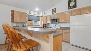 Una cocina con armarios de madera, un refrigerador blanco, un microondas y una zona de bar con sillas de madera.