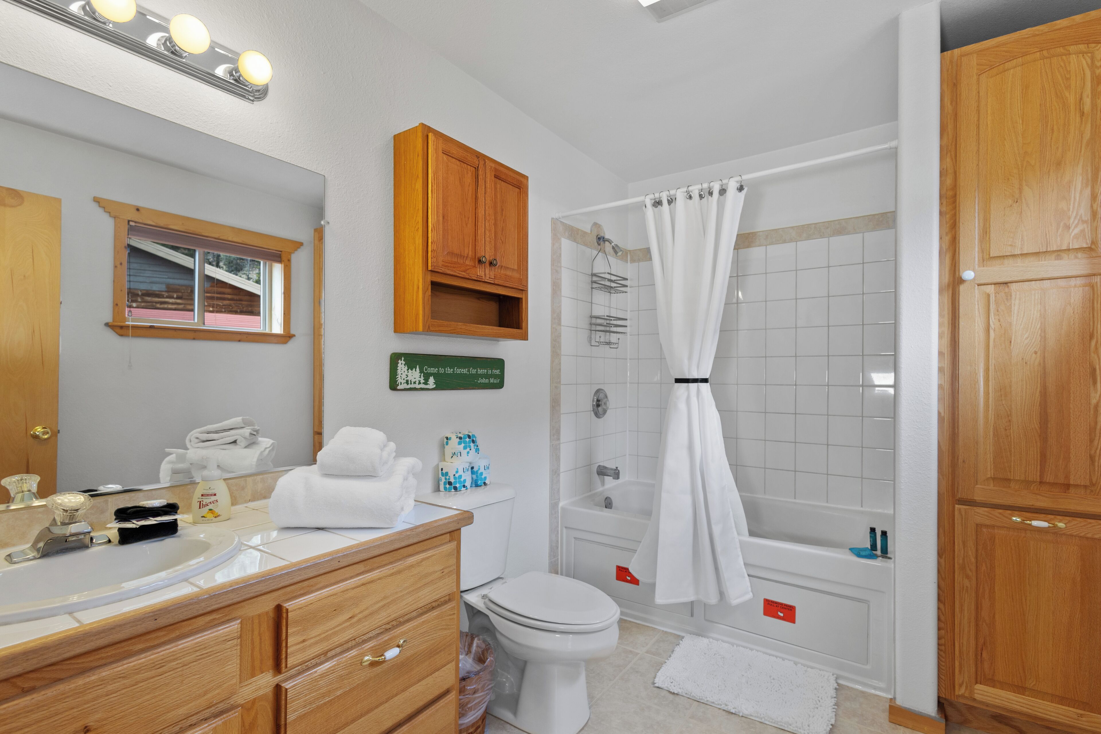 A bathroom with a wooden vanity, a toilet, a bathtub, and a shower curtain.