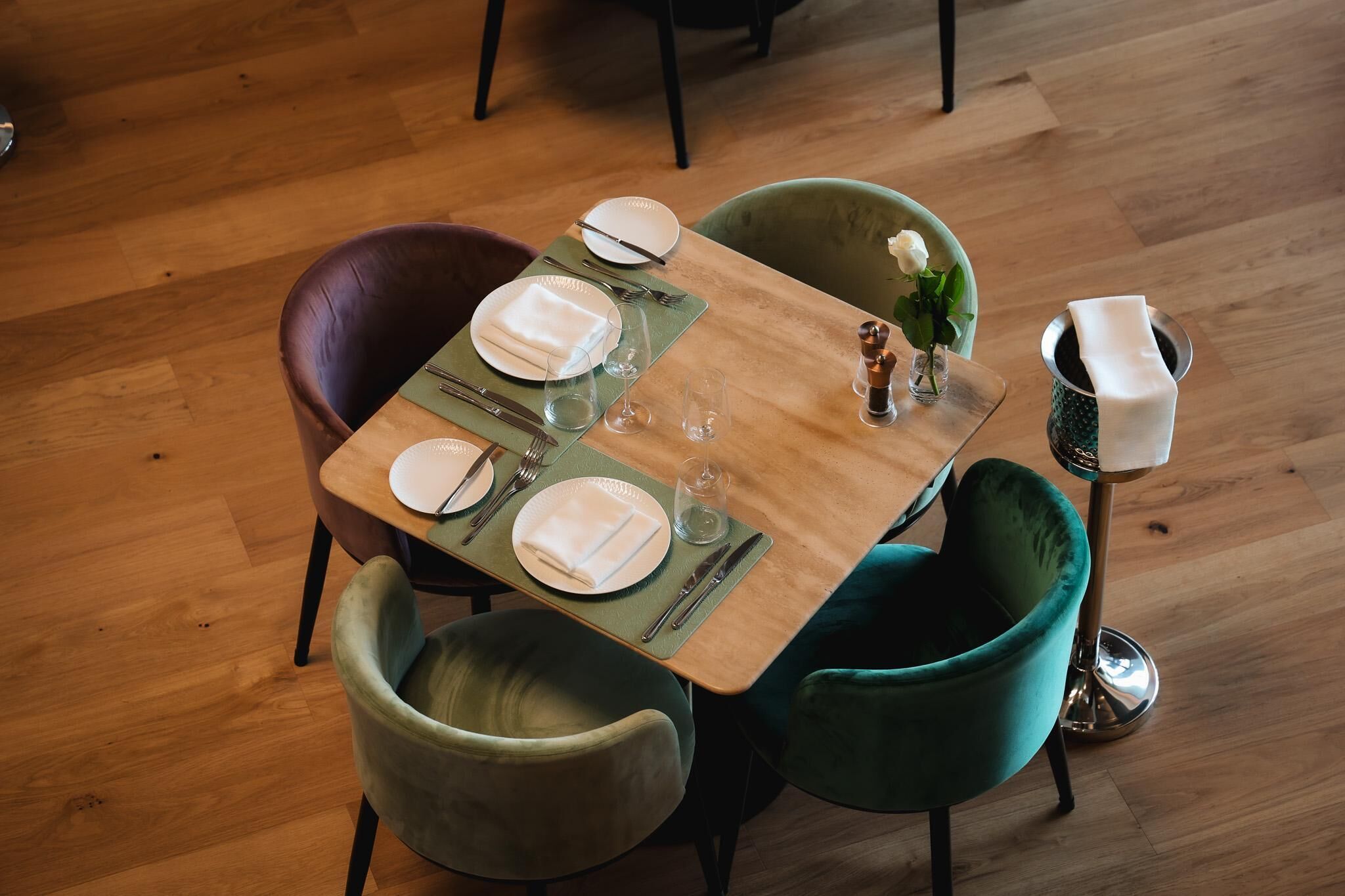 Una mesa de comedor dispuesta con platos, cubiertos y vasos, rodeada de sillas.