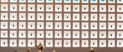 Un interior moderno con una pared de frascos de perfume iluminados, mesas redondas y sillones de terciopelo.