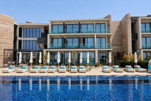 Un hotel moderno con piscina, varias zonas de descanso y un cielo azul despejado.