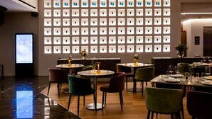 Un interior moderno con una pared de vitrinas iluminadas, un área de comedor con mesas y sillas redondas, y un reloj digital que muestra la hora.
