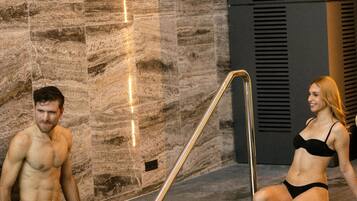 A man and a woman in a spa pool area with stone walls and a metal staircase.