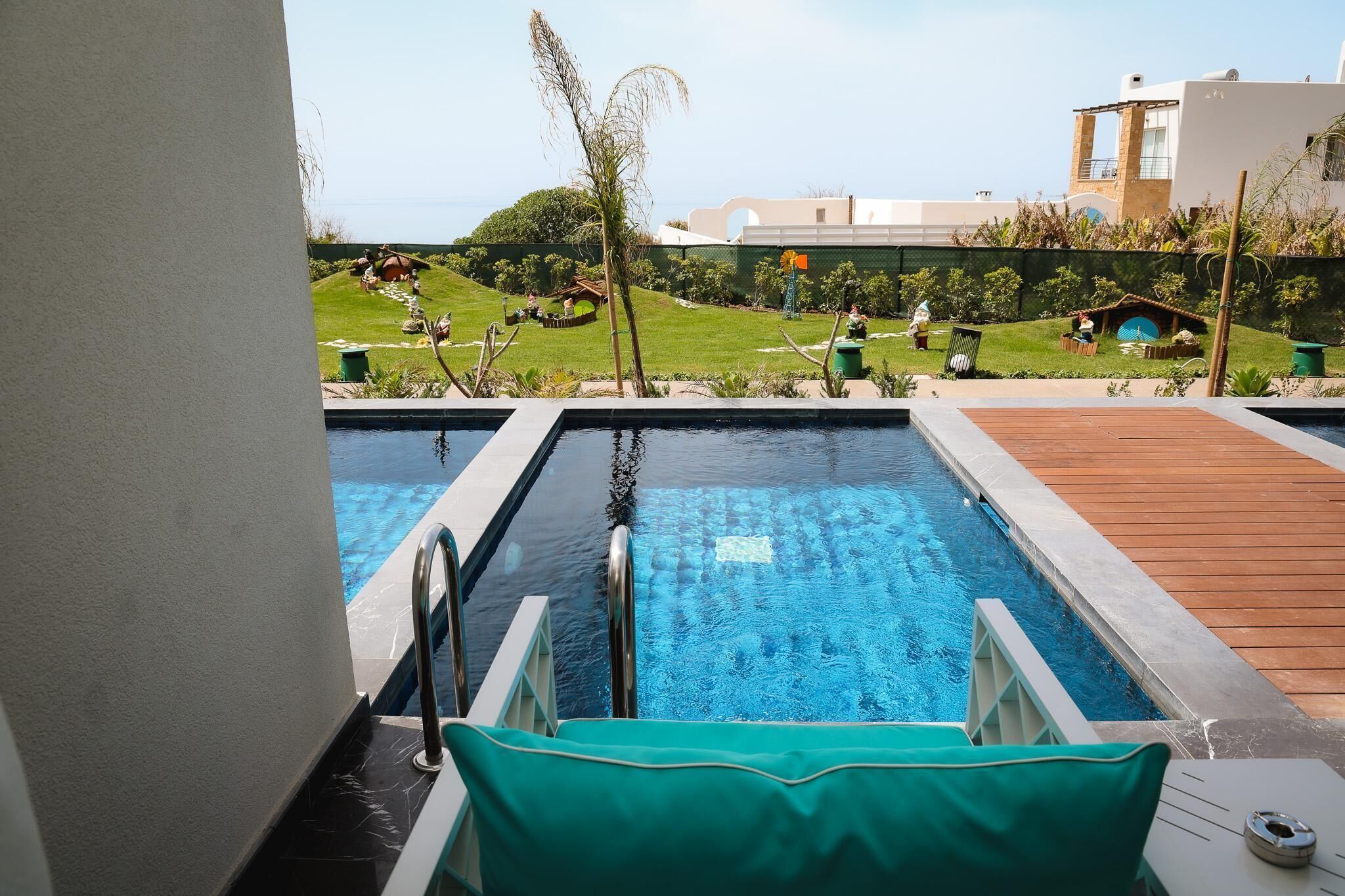 A swimming pool with a wooden deck, surrounded by a well-maintained lawn and a building in the background.
