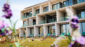 Un hotel moderno con varios balcones, un jardín cuidado y zonas de estar al aire libre.