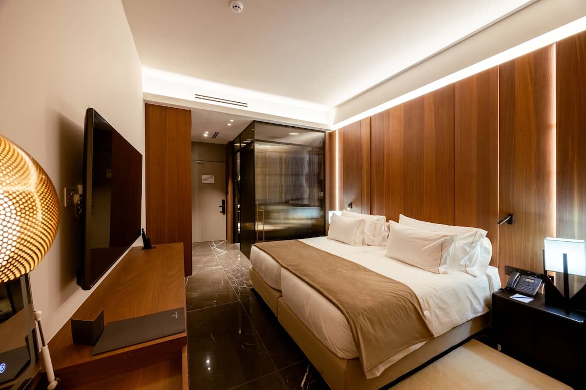 Habitación de hotel moderna con una cama grande, un televisor de pantalla plana, un escritorio con lámpara y un panel de pared de madera.