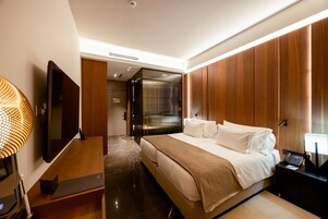 Habitación de hotel moderna con una cama grande, un televisor de pantalla plana, un escritorio con lámpara y un panel de pared de madera.