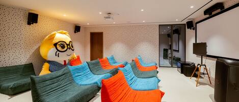 A modern room with a large plush toy, multiple bean bag chairs, a projector screen, and a speaker system.