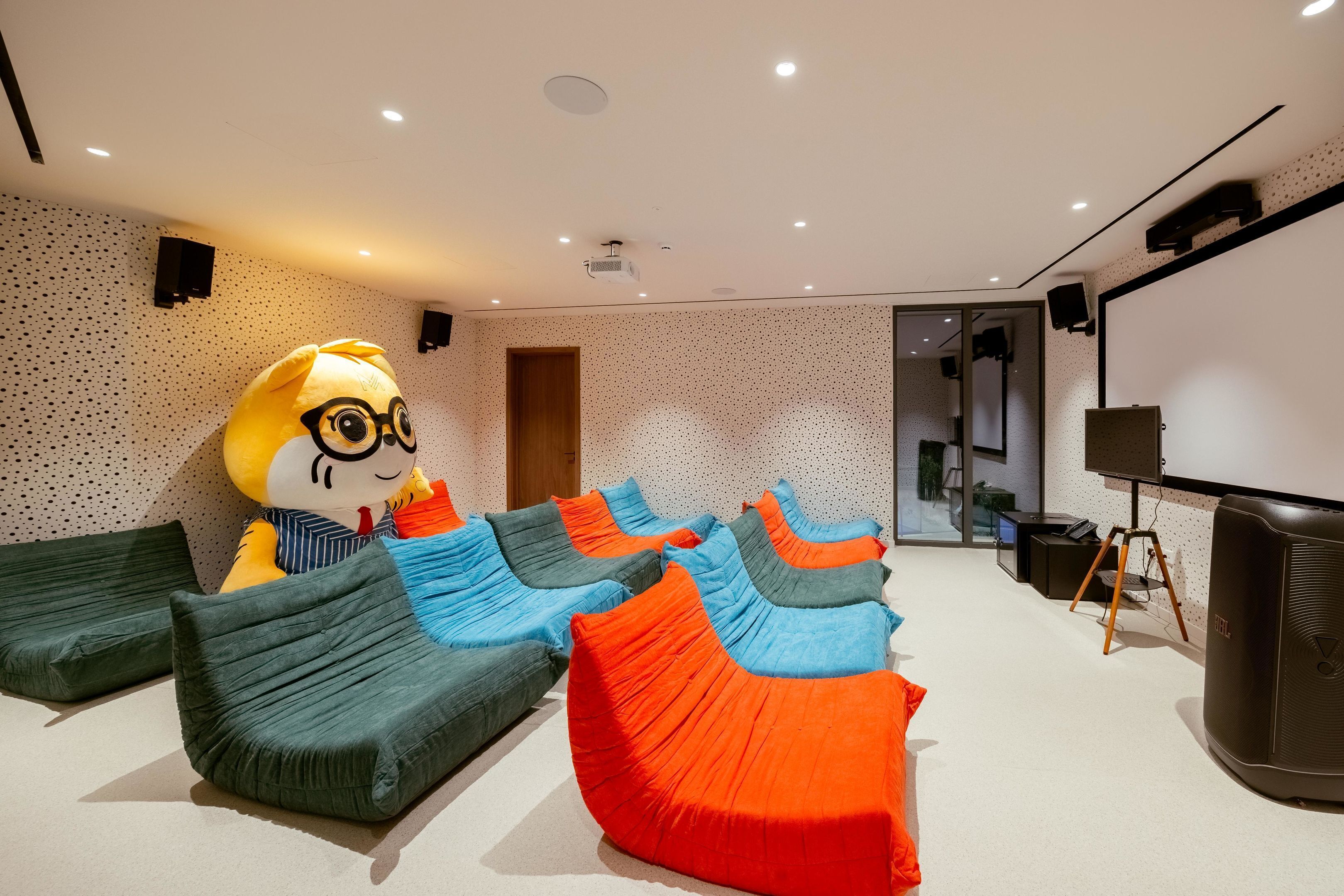 Een kamer met loungen in een zak, een groot mascottebeeld, een projectiescherm en een geluidsinstallatie.
