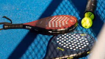 A tennis racket, two tennis balls, and a tennis ball container on a blue textured surface.