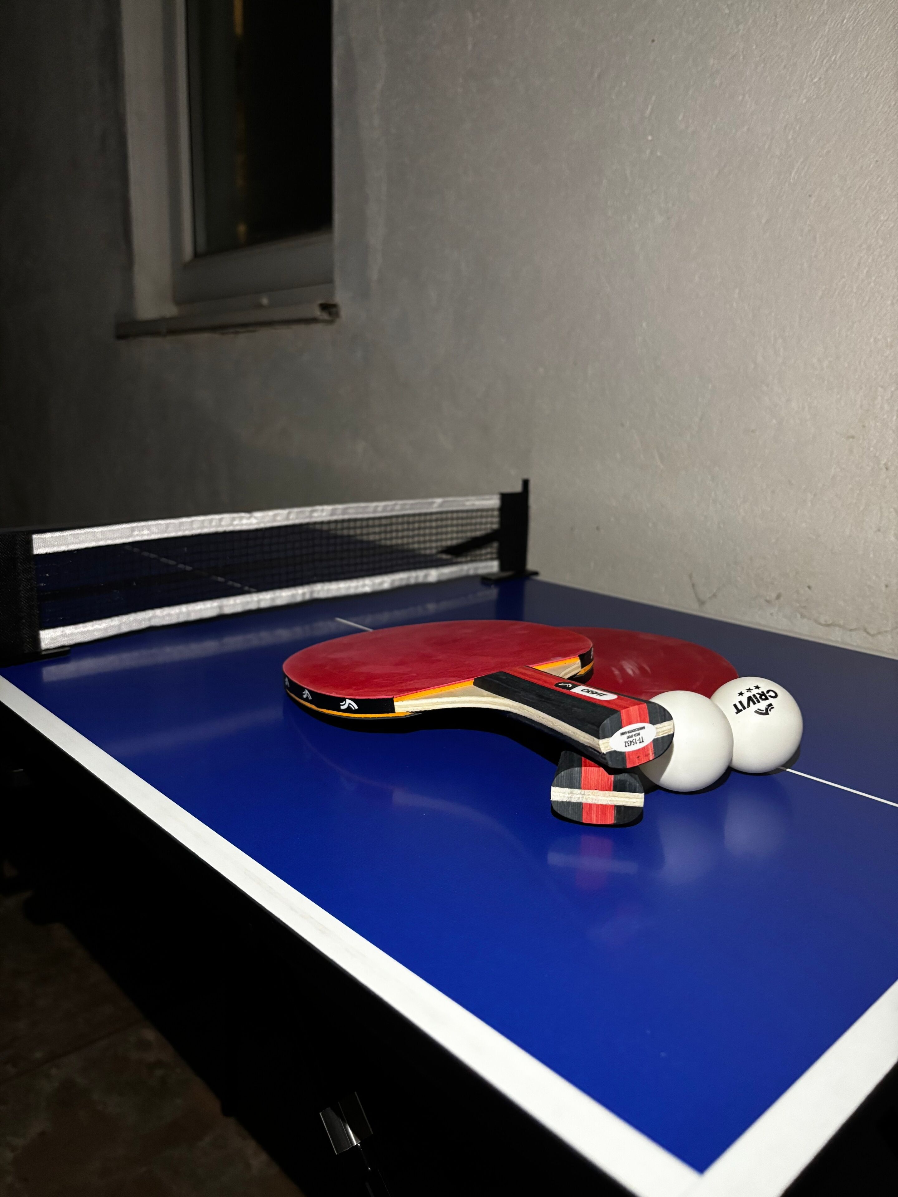 A ping pong table with a red paddle and two white balls.