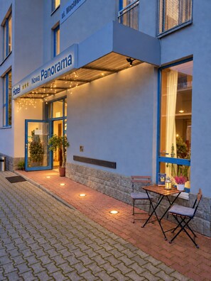 Entrada de hotel con un letrero que dice 'Hotel Panorama', asientos exteriores y un muro de piedra.