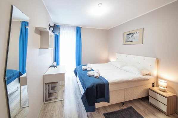 A neatly arranged bedroom with a bed, bedside tables, a desk, and a mirror.