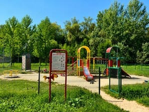 Un parque infantil con diversas estructuras de juego, rodeado por una cerca y follaje.