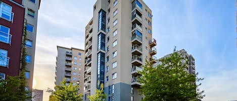 Un edificio residencial alto con varios balcones, rodeado de vegetación y vehículos estacionados.