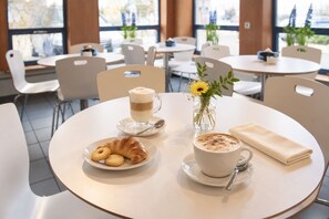 Una mesa redonda con un croissant, una taza de café y un pequeño jarrón con flores.