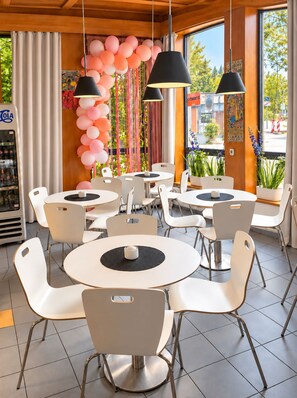 A restaurant interior with round tables and white chairs, a soda machine, and a view of the street through large windows. - Hotel Nowa Panorama Double Room with BB and Free WiFi (Kraków)