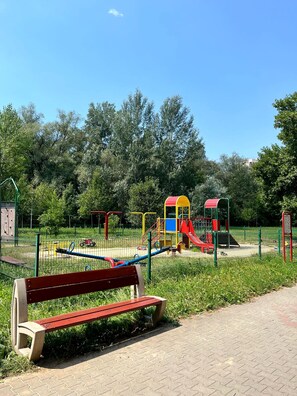 Une aire de jeux avec un banc rouge, une structure d’escalade et un toboggan.