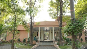 Un bâtiment doté d’une entrée centrale, entouré d’un jardin agrémenté de diverses plantes et d’une fontaine.