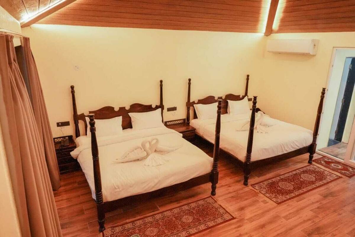 Ein Zimmer mit zwei hölzernen Betten mit Säulen, Holzboden und Deckenbalken.