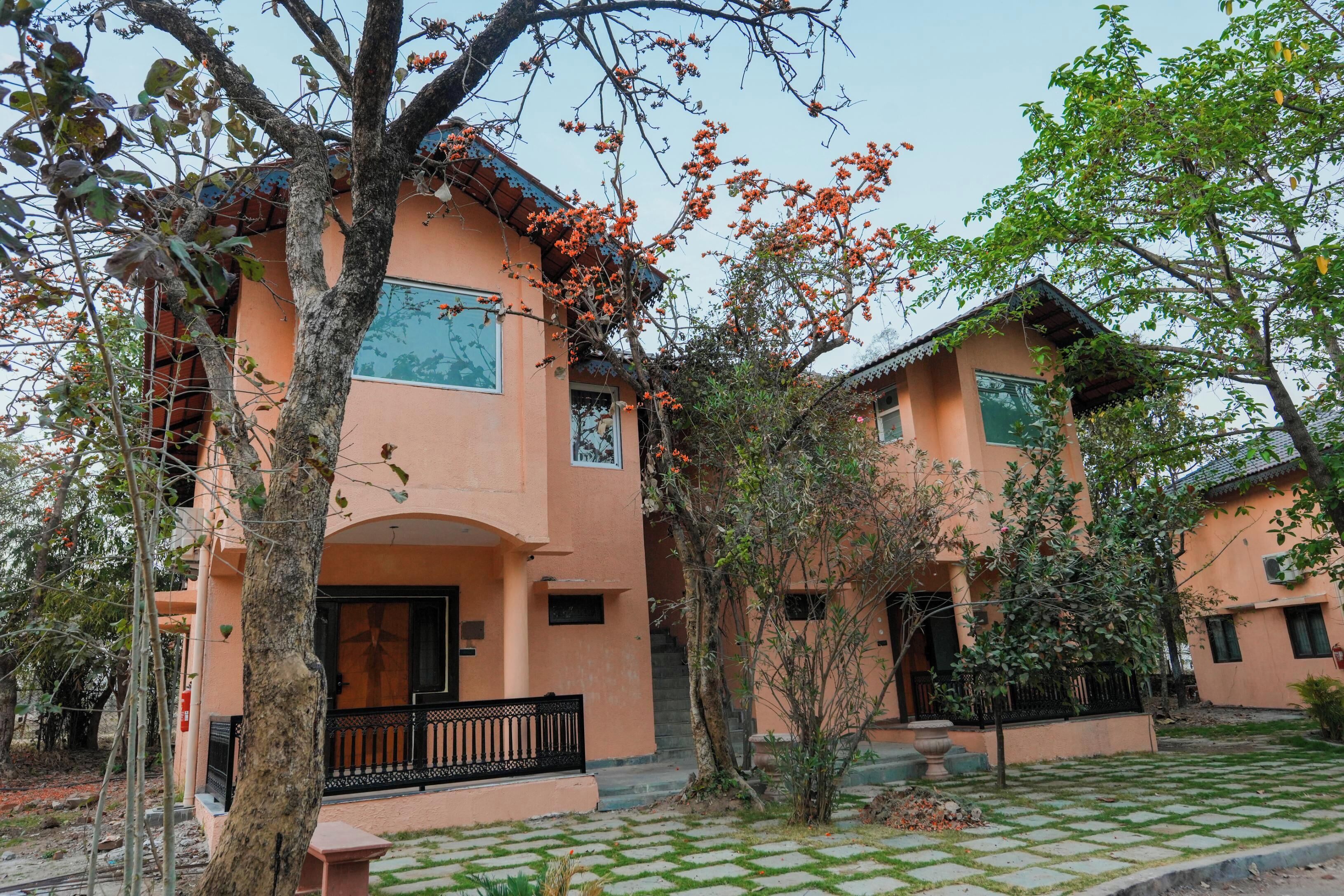Un edificio de dos pisos con un patio a cuadros, un balcón y un árbol con flores naranjas.